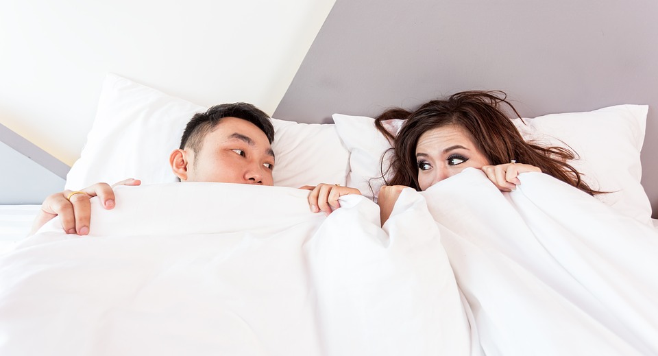 a man and woman laying in bed under covers