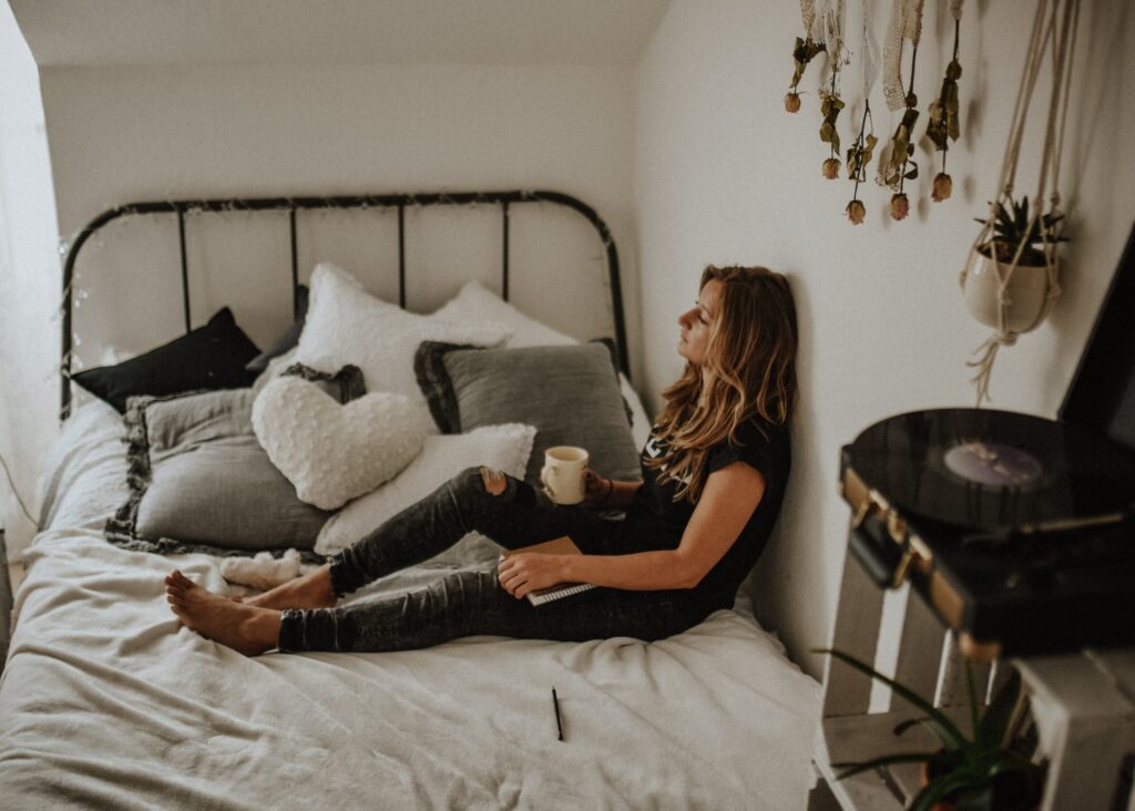 a woman is sitting on her bed drinking coffee