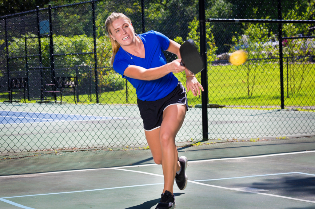 a woman in blue shirt and black shorts playing pickleball